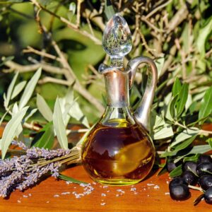 Glaskaraffe mit Salböl zwischen Oliven und Kräutern